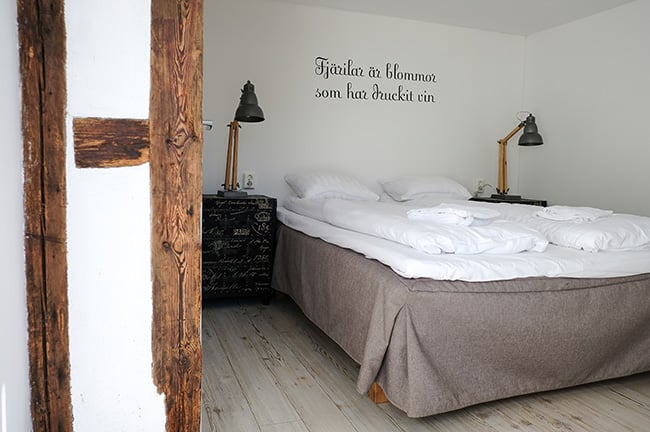 Hotellrum med säng, på Arilds vingård i Skåne. På den vita väggen ovanför sängen står ett citat: "Fjärilar är blommor som har druckit vin."