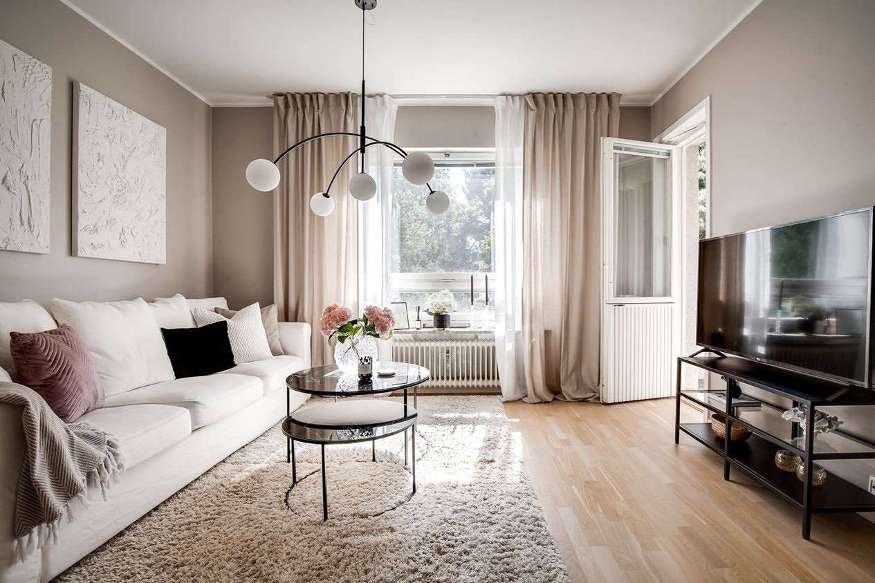 Bostadsrätt – vardagsrum med stor vit soffa och härliga ryamattor